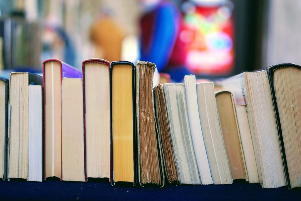 A row of well-read hardback and paperback books standing upright on a shelf, seen from the page edges.
