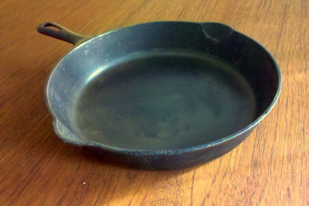 An old, well-worn cast iron skillet sitting empty on a wooden table.