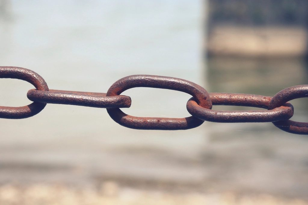 A close-up of a rusty metal chain stretched horizontally against a soft blurred background.