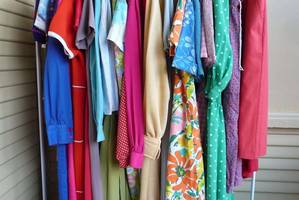 Colourful vintage dresses and blouses in florals, polka dots and solid colours hanging on a white clothes rack.
