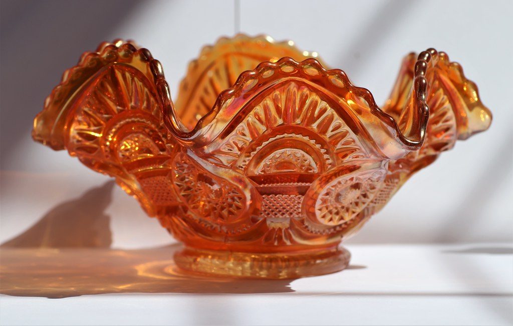 An iridescent marigold carnival glass bowl with ruffled edges, sunlit on a white surface.