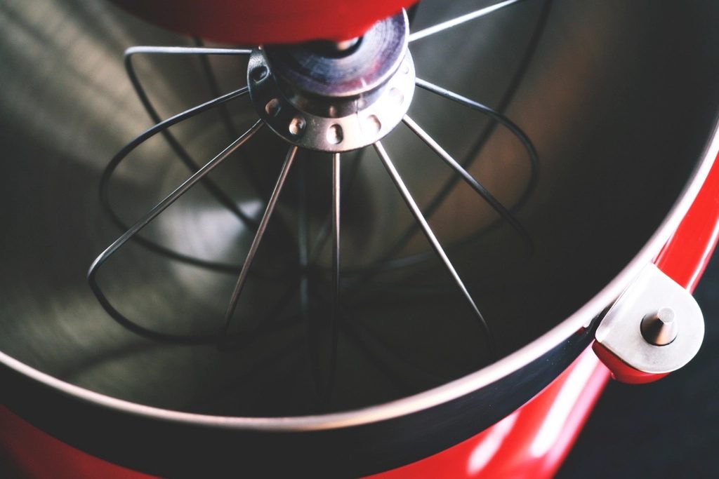 Close-up looking into the steel bowl of a red stand mixer with its wire whisk attachment.