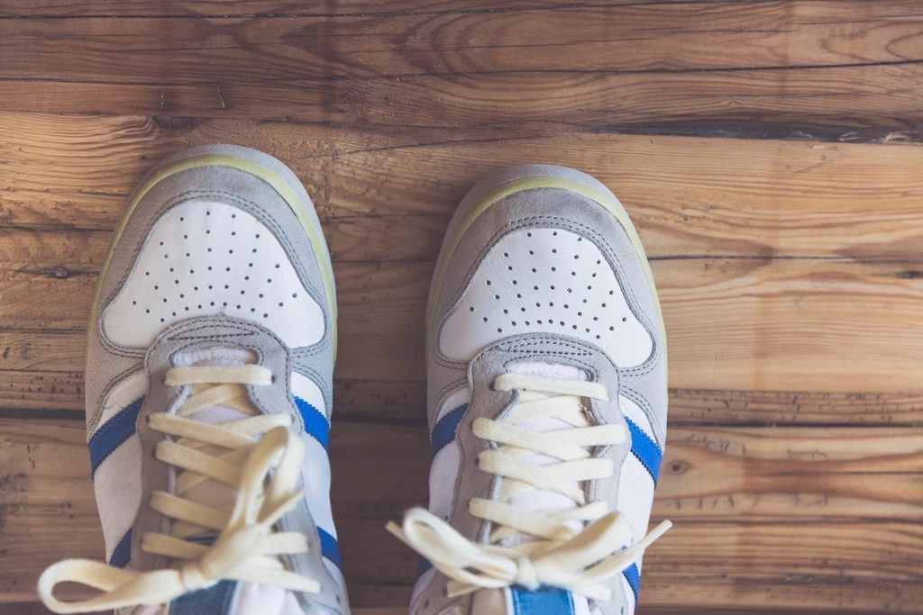 A pair of white, grey and blue laced sneakers seen from above on a weathered wooden floor.